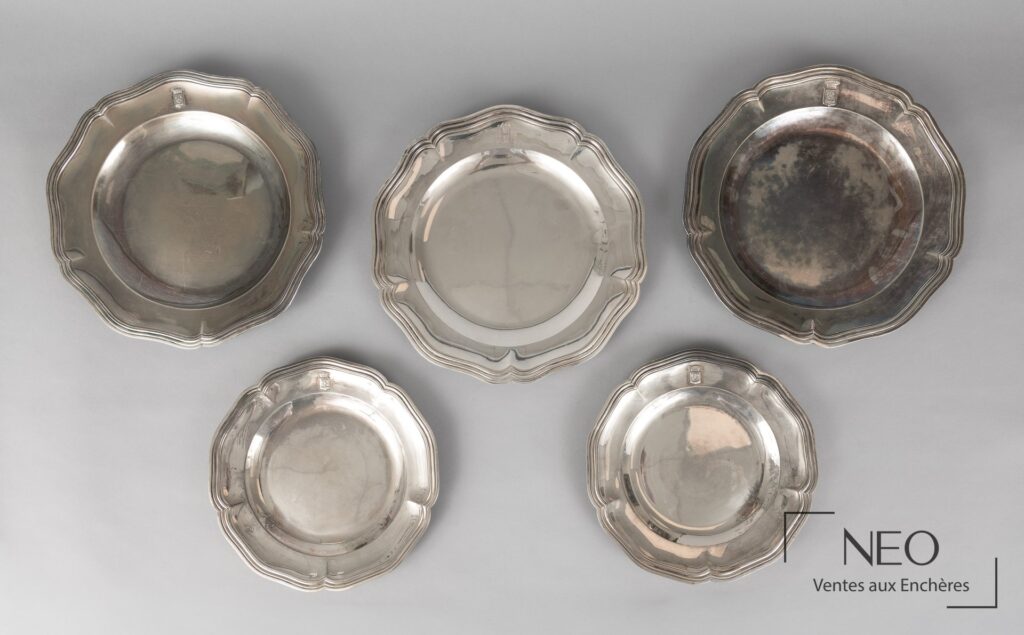 Cinq plats en argent à bords chantournés disposés sur fond gris