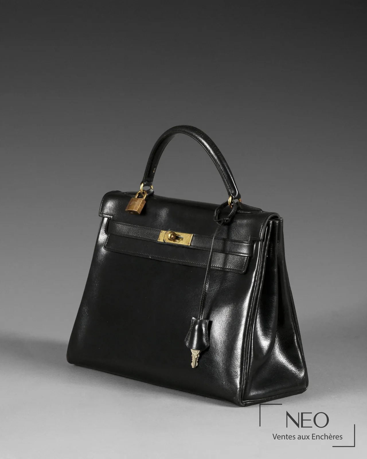 Profil d'un sac Kelly Hermès 32 en box noir : sanglons, touret et emplacement de la lettre date